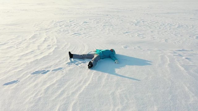 A girl makes a figure of a snow angel in a clearing in the forest. Aerial photography of a girl lying in the snow.