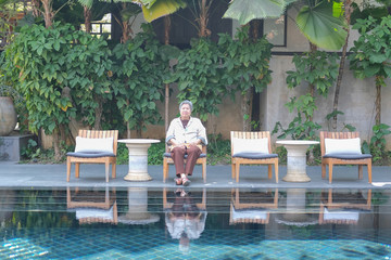 old elderly senior elder woman resting relaxing at poolside of swimming pool in hotel