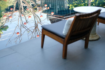 tree reflection on swimming pool with wooden chair in hotel  for relaxing at poolside