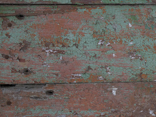 Texture. Fragment of an old wooden wall covered with cracked red, brown and light green paint. Close-up.