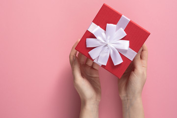 Valentine's Day celebration concept. A nice gift from a loved one. Box with a bow in female hands on a delicate pink background. Copy space. Flat lay.