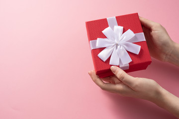 Valentine's Day celebration concept. A nice gift from a loved one. Box with a bow in female hands on a delicate pink background. Copy space. Flat lay.