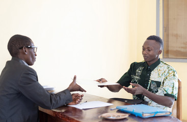 Candid photo of African black job application form being handed over to business man interviewer in...