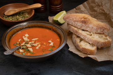 Vegan roasted pepper and tomato soup along with chiabatta bread on dark backround
