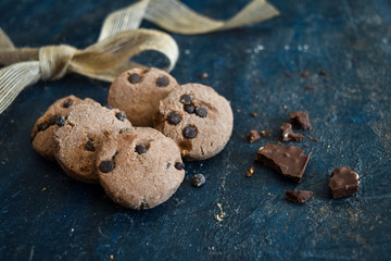 Chocolate chip cookies with ribbon and dark chocolate on a rustic blue background. Fresh, homemade, baked, gluten free, vegan concepts. Close up of a pile of choco chip cookies with space for text.
