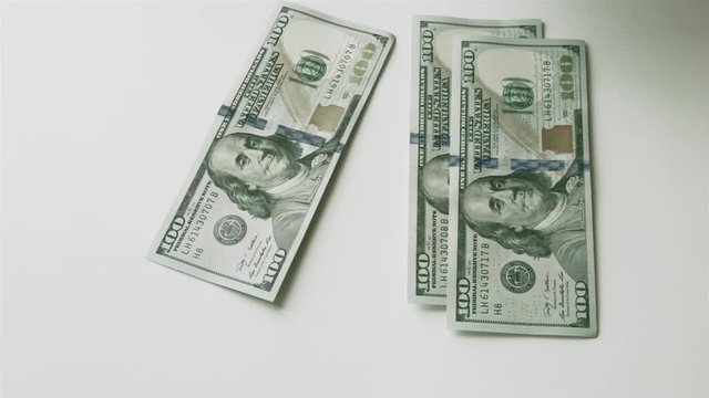 Splitting money into two equal stacks. Men's hand puts hundred-dollar bills on the table, and then takes them away.