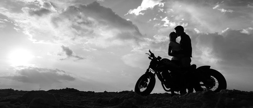 Silhouettes of a couple in love with a motorcycle on the background of the sunset sky