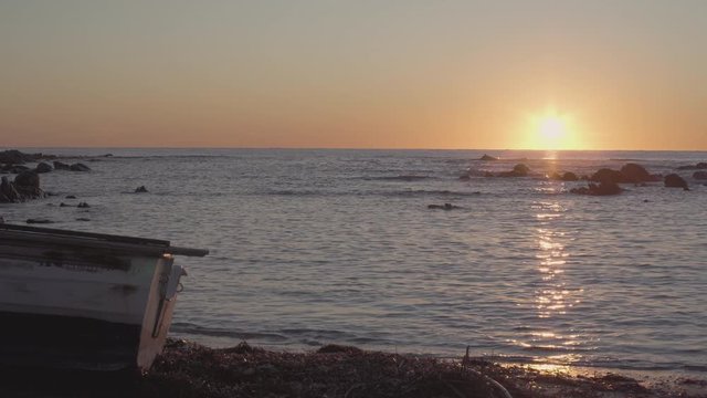 Wooden boat on the beach at dawn or dusk with small waves of the sea and reflection of the sun in the water - prores log