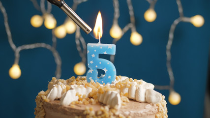 Birthday cake with 5 number candle on blue backgraund set on fire by lighter. Close-up