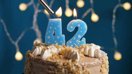 Birthday cake with 42 number candle on blue backgraund set on fire by lighter. Close-up
