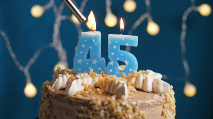Birthday cake with 45 number candle on blue backgraund set on fire by lighter. Close-up