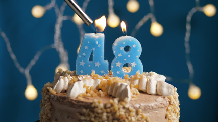 Birthday cake with 48 number candle on blue backgraund set on fire by lighter. Close-up