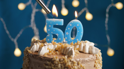 Birthday cake with 50 number candle on blue backgraund set on fire by lighter. Close-up