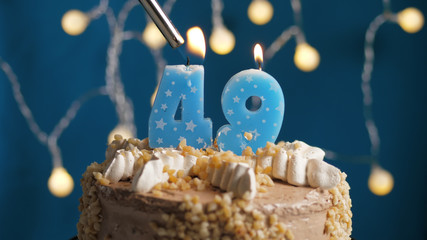 Birthday cake with 49 number candle on blue backgraund set on fire by lighter. Close-up