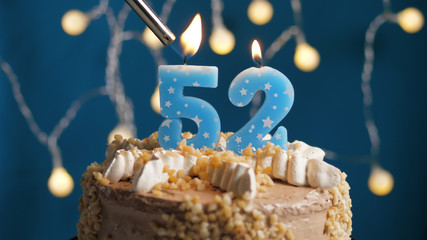 Birthday cake with 52 number candle on blue backgraund set on fire by lighter. Close-up