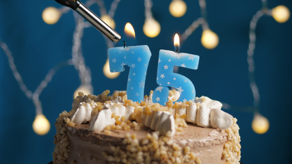 Birthday cake with 75 number candle on blue backgraund set on fire by lighter. Close-up