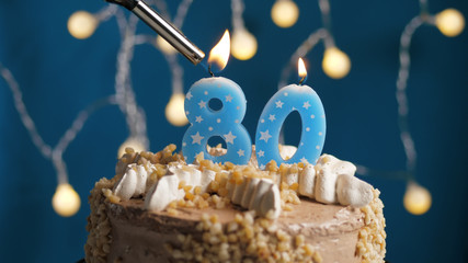 Birthday cake with 80 number candle on blue backgraund set on fire by lighter. Close-up