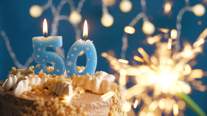 Birthday cake with 50 number candles and burning sparkler on blue backgraund. Close-up