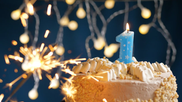 Birthday cake with 1 number candles and burning sparkler on blue backgraund. Close-up
