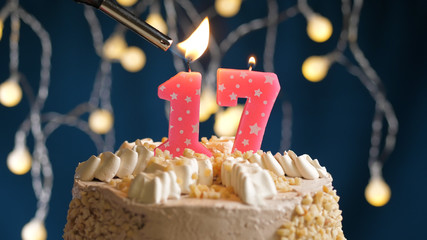 Birthday cake with 17 number candle on blue backgraund set on fire by lighter. Close-up view