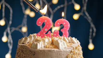 Birthday cake with 23 number candle on blue backgraund set on fire by lighter. Close-up view