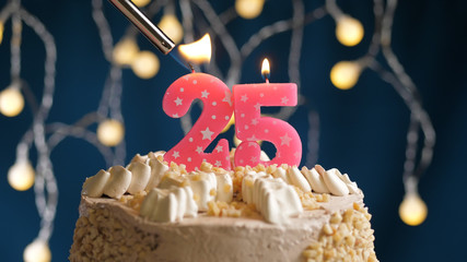 Birthday cake with 25 number candle on blue backgraund set on fire by lighter. Close-up view