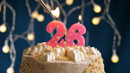 Birthday cake with 26 number candle on blue backgraund set on fire by lighter. Close-up view
