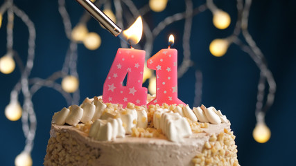 Birthday cake with 41 number candle on blue backgraund set on fire by lighter. Close-up view