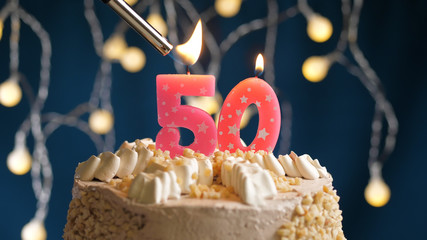 Birthday cake with 50 number candle on blue backgraund set on fire by lighter. Close-up view