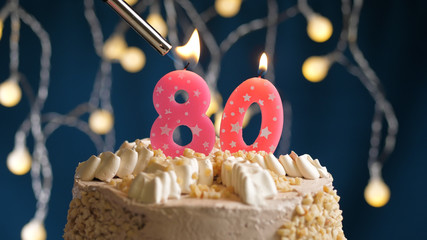 Birthday cake with 80 number candle on blue backgraund set on fire by lighter. Close-up view