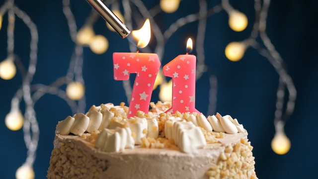 Birthday cake with 71 number candle on blue backgraund set on fire by lighter. Close-up view