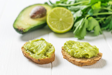 Two thin slices of bread with guacamole on a white wooden table. Diet vegetarian Mexican food avocado.