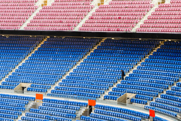 Empty stands of a stadium with empty seats of blue and red, and a maintenance person