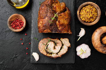 Roast pork meat roll  with herbs and spices on black stone table.