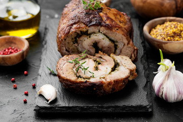 Roast pork meat roll  with herbs and spices on black stone table.