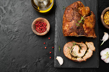Roast pork meat roll  with herbs and spices on black stone table.