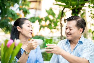 Senior couple with food and drink picnic in garden park talking care together
