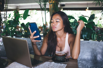 Relaxed Asian lady texting on smartphone at cafe