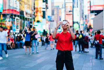 Caucasian female standing in crowded square with mobile phone in hands.Addicted to social network. Millennial technology user. Young woman browsing internet via app on smartphone. Tourist explore city