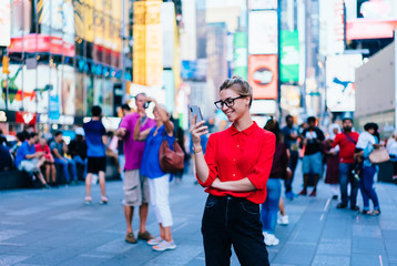 Caucasian female standing in crowded square with mobile phone in hands.Addicted to social network. Millennial technology user. Young woman browsing internet via app on smartphone. Tourist explore city