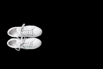 Short white low brigt sneakers on a black background. 