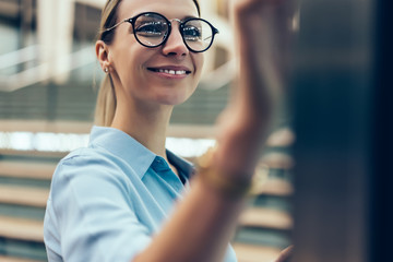 Smiling female standing at innovative display with advanced digital technology. Young woman touching with finger futuristic screen of interactive kiosk for find information while standing outdoors
