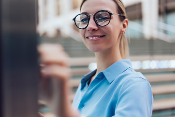 Smiling female standing at innovative display with advanced digital technology. Young woman touching with finger futuristic screen of interactive kiosk for find information while standing outdoors