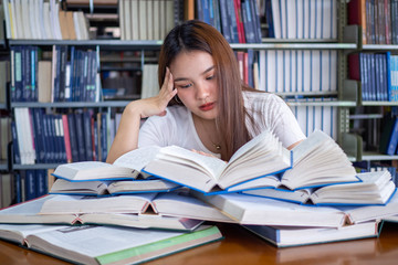 Female students are stressed with reading a lot of books placed on the tables in the library. To prepare for the exam