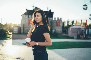 Serious asian female student in casual wear making mobile phone call while walking on city street during free time at summer evening,thoughtful hipster girl waiting for making roaming connection .