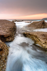Sunrise with water flowing over rocks in the ocean