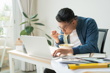 Cheerful engineer with dessert sitting in front of computer monitor and eating noodle