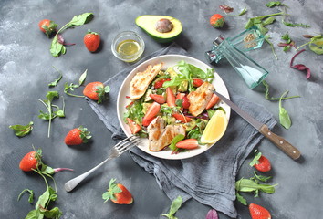 Chicken salad with avocado, strawberries,blue cheese, arugula, beet leaves. Healthy lunch avocado bowl, plate with chicken and strawberries on the dark gray background. Healthy food concept.