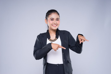 An attractive woman wearing business attire with gestures towards copyspace area isolated on grey....