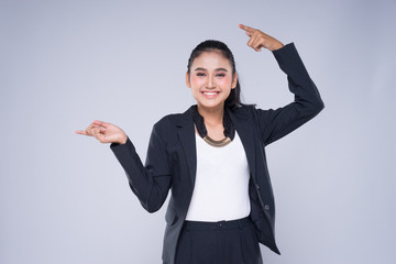 An attractive woman wearing business attire with gestures towards copyspace area isolated on grey....